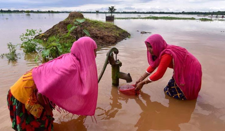 Women collect drinking water from a hand pump in a flood-hit area, at Madhabpara village in Nagaon district of Assam | PTI